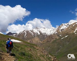 the two men are walking at the mountains of alamut valley with snow at peaks