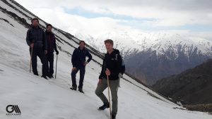 four men are walking on the snow with a background of snow-peaked mountains